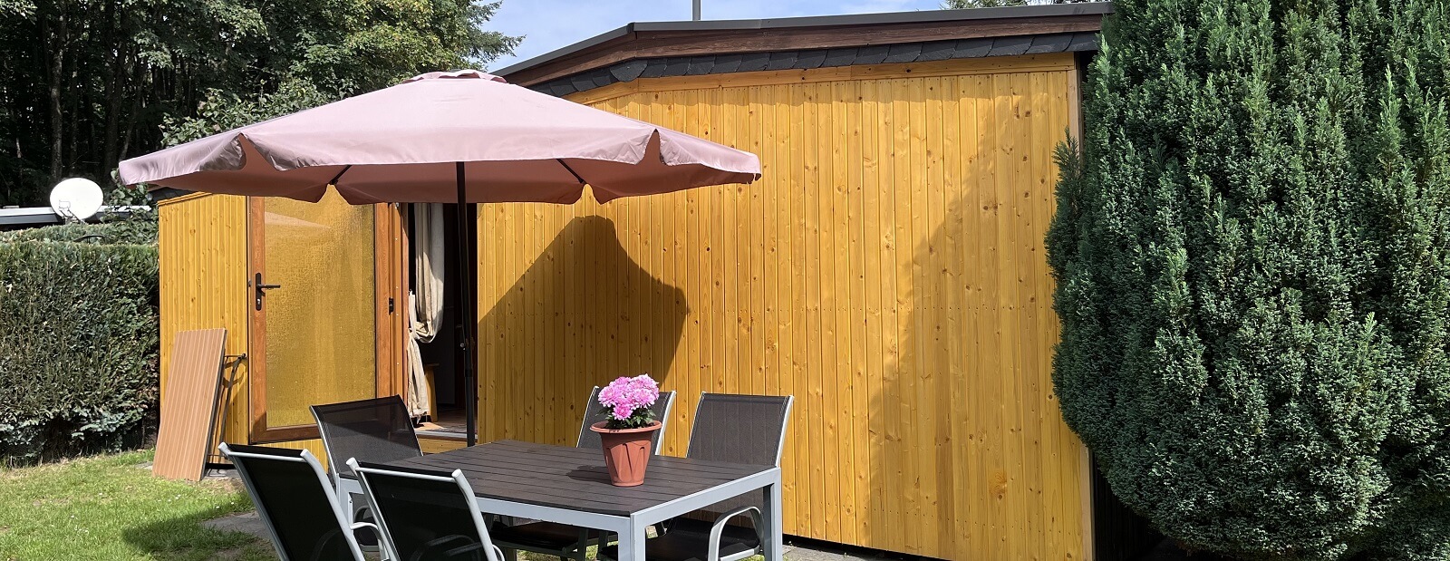 Außenansicht eines Holzbungalows mit Tisch, Stühlen und Sonnenschirm