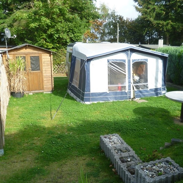 Parzelle mit Wohnwagen und Vorzelt und einer Holzhütte und seitlichem Holzzaun