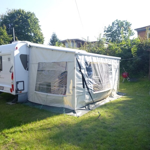 Moderner Wohnwagen mit Vorzelt auf einer Parzelle mit Rasen und Hecken am Rand